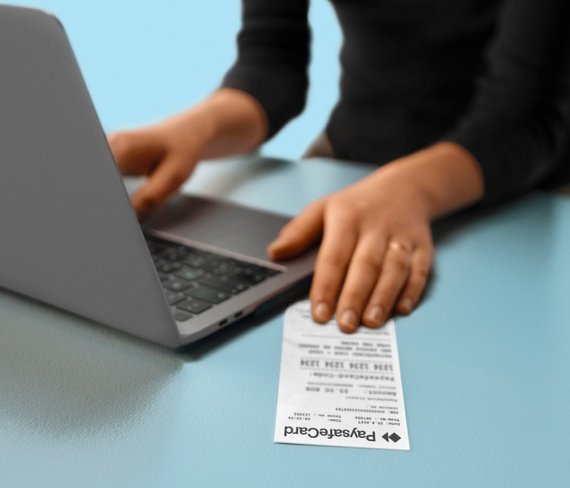 Person using laptop with PaysafeCard receipt on table