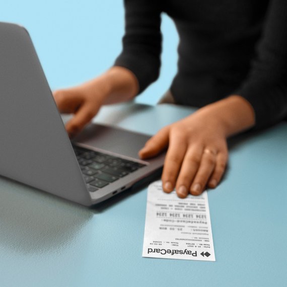 A person using a laptop with a PaysafeCard receipt on the table