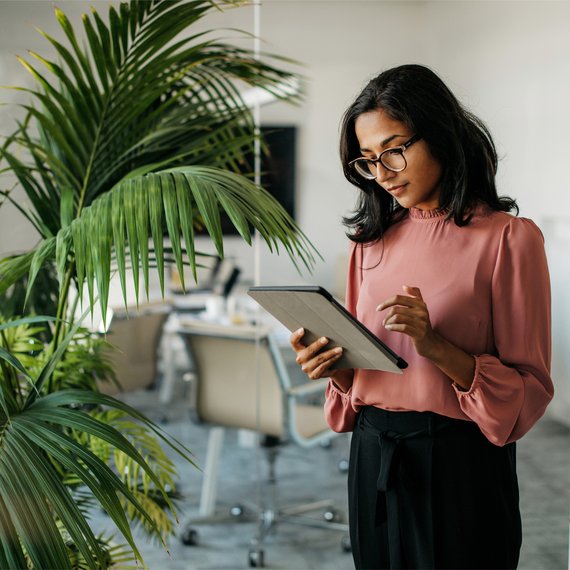 Woman in beige top standing and reading something on the tablet