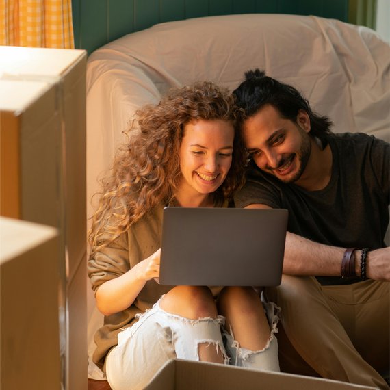 Couple sitting together on the floor reading something from their laptop, smiling