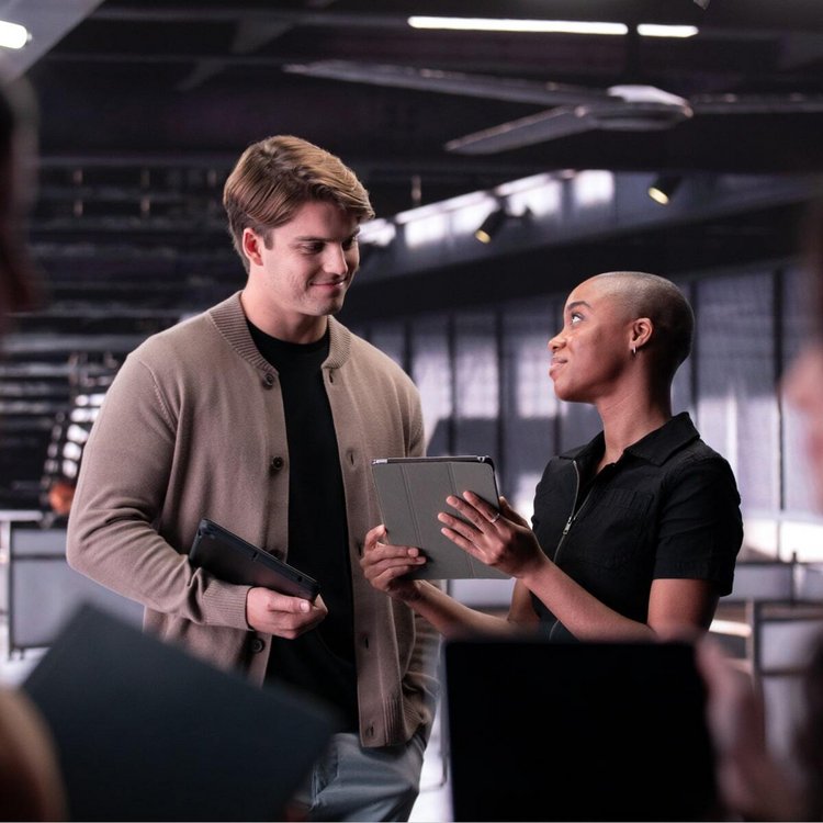 Two individuals in office, one with folder, other with tablet