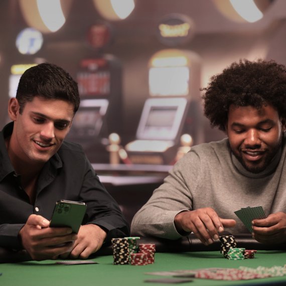 Two individuals at poker table with smartphone and cards