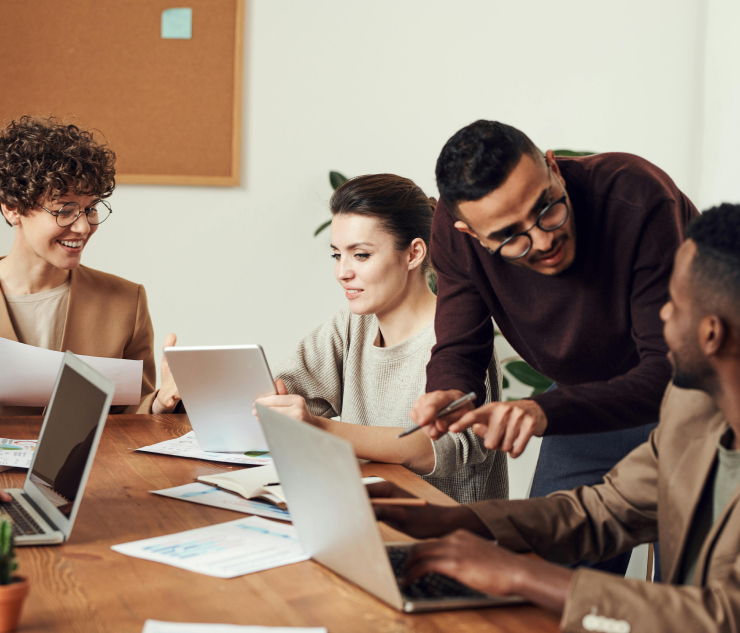 Group of individuals at table with laptops, papers scattered