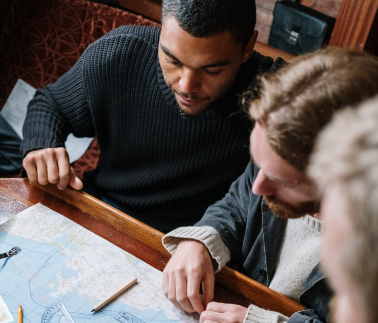 Three individuals planning a route with map and pencils on table