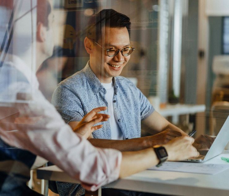 Two individuals at desk with laptop, office setting