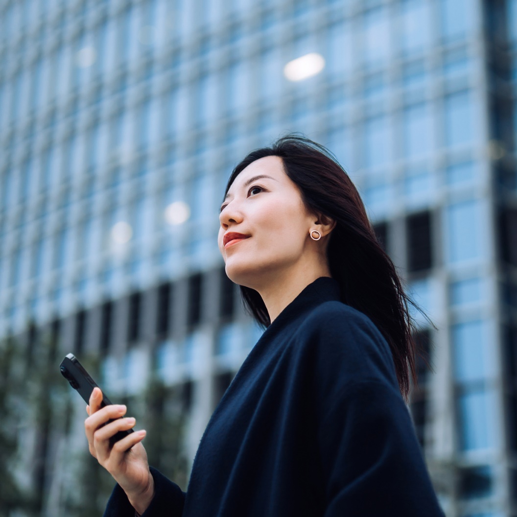 Individual from side with phone, standing by reflective building
