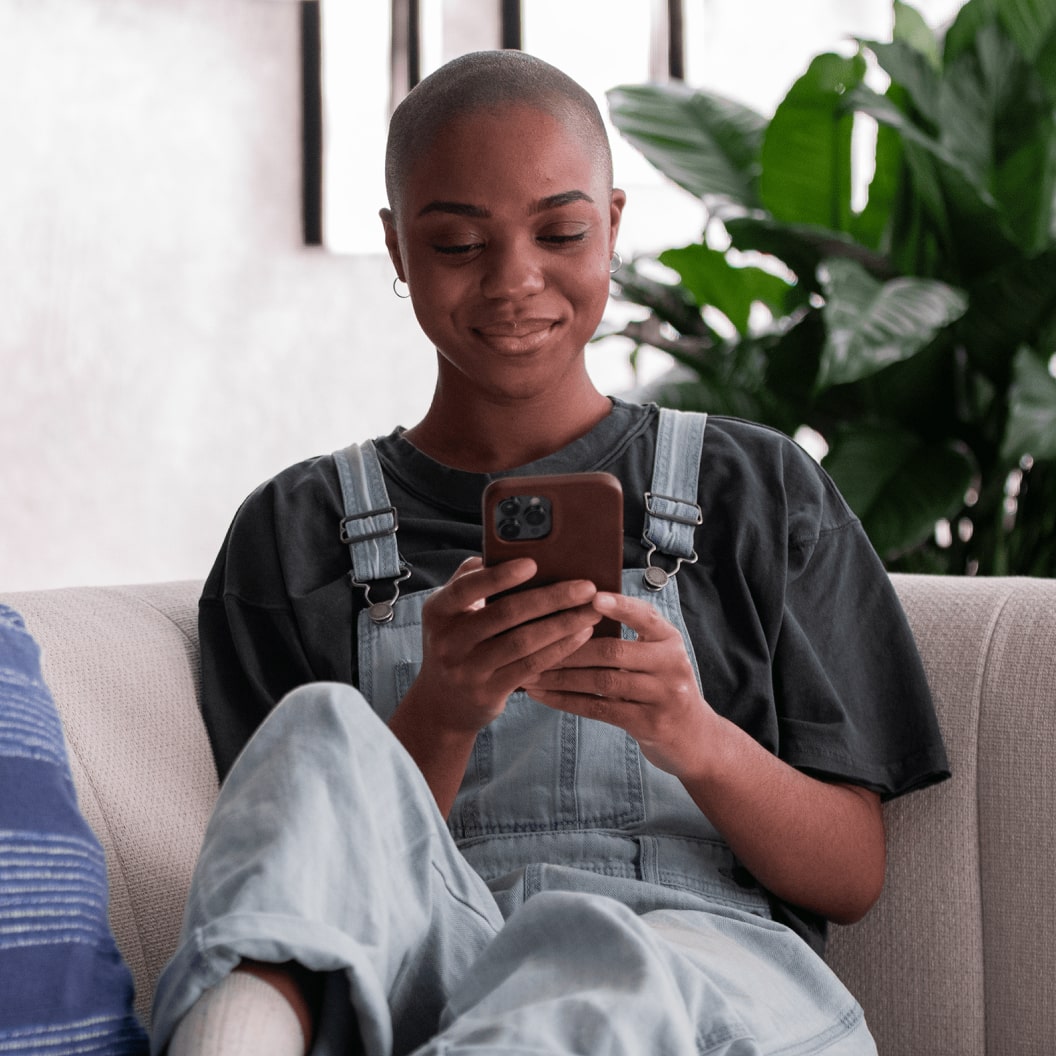 Person in overalls using smartphone on couch