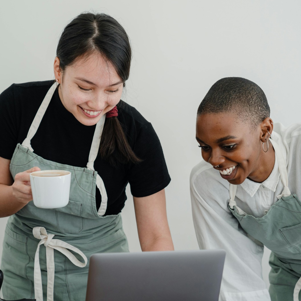 Two individuals, one with a cup, the other using a laptop