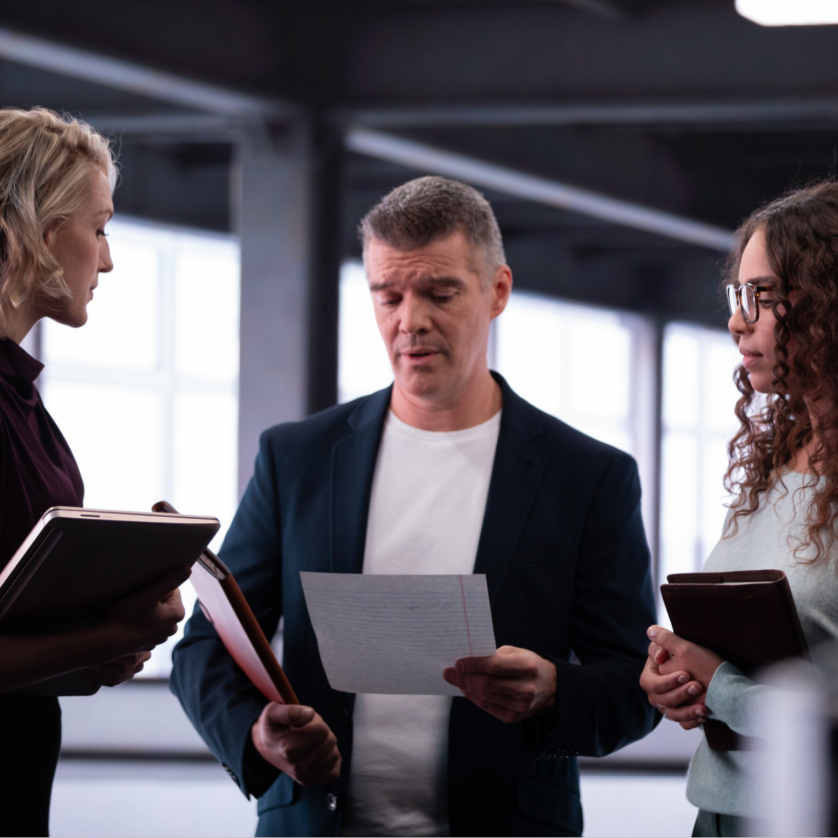 Three individuals standing and interacting holding paper documents