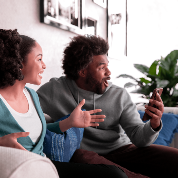 Two individuals sitting on a couch, one gesturing with a smartphone
