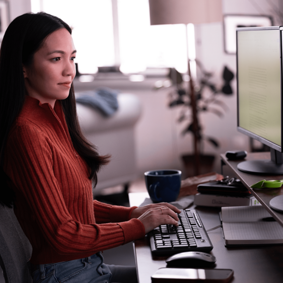 Individual at desk with computer setup, orange top, and cup