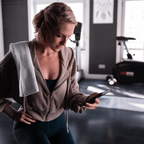 Person in gym holding phone with towel on shoulder